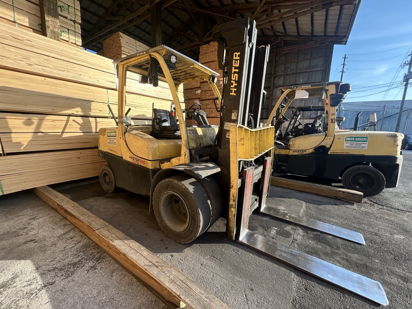 Yellow forklift moving a stack of lumber under a shed