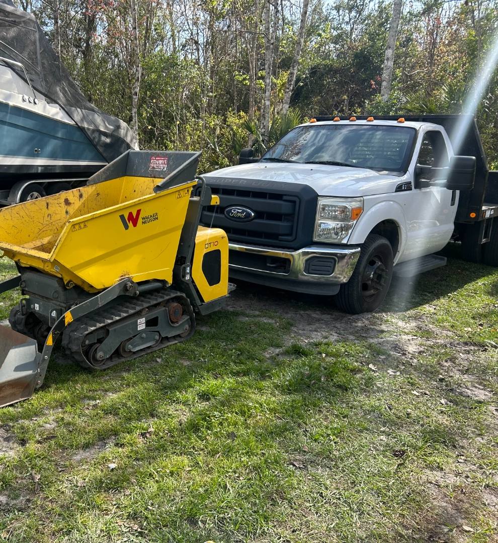 Yellow tracked compact dumper parked beside a work truck on grass