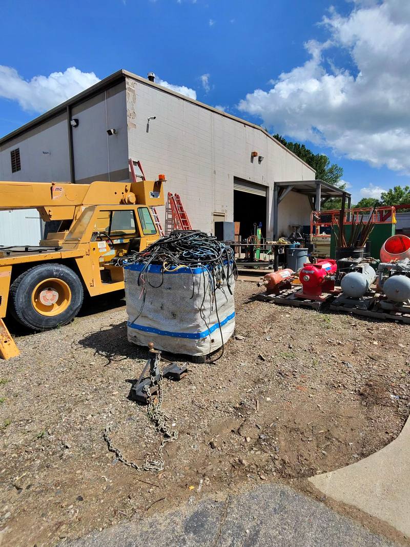 Industrial yard with a lift, a bagged bundle of cable, and mixed surplus outside a warehouse